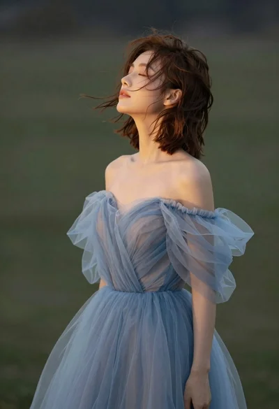 Young woman in blue tulle gown standing with eyes closed in wind