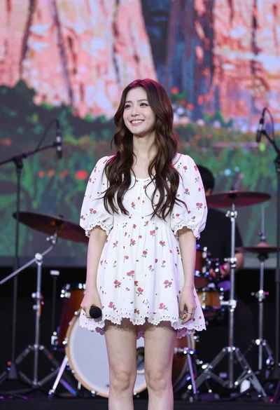 Smiling woman in floral mini dress holding microphone on concert stage