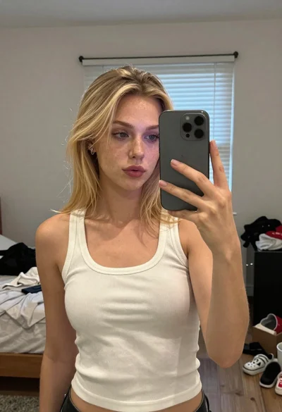 Woman with blonder hair taking mirror selfie in messy bedroom