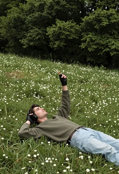 Man lying in grassy meadow pointing skyward with forest background