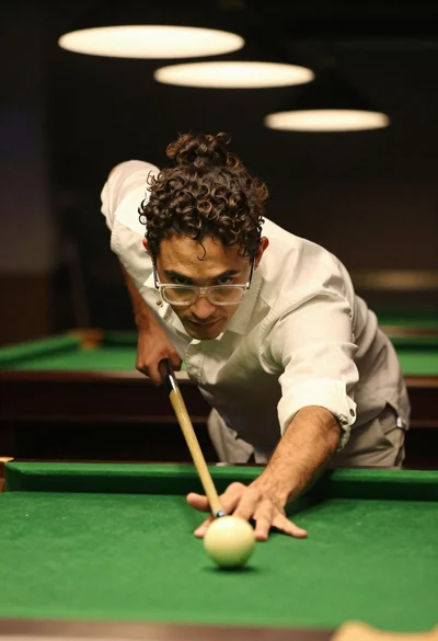 Young man aiming pool cue over green table in dimly lit bar