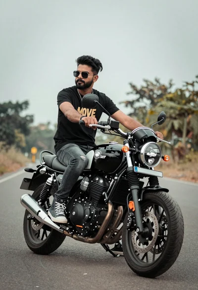 Man sitting on black motorcycle on paved road under cloudy sky