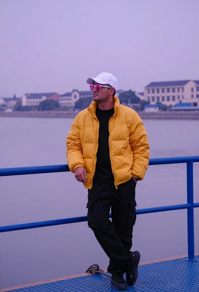 Man in yellow puffer jacket on blue dock overlooking water and buildings