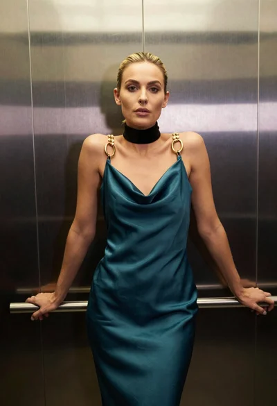 Blonde woman in teal slip dress leaning on elevator handrail