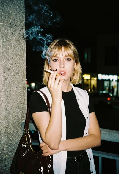 Portrait of blonde woman with cigarette on concrete balcony at night