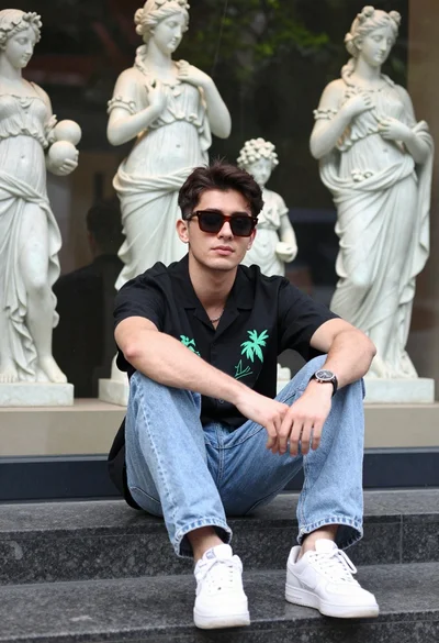 Young man sitting on stone ledge near classical statue display case