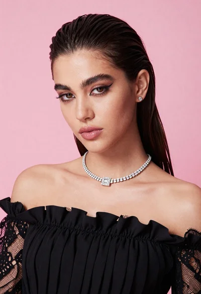 Glamorous portrait of young woman in black ruffled top against pink background