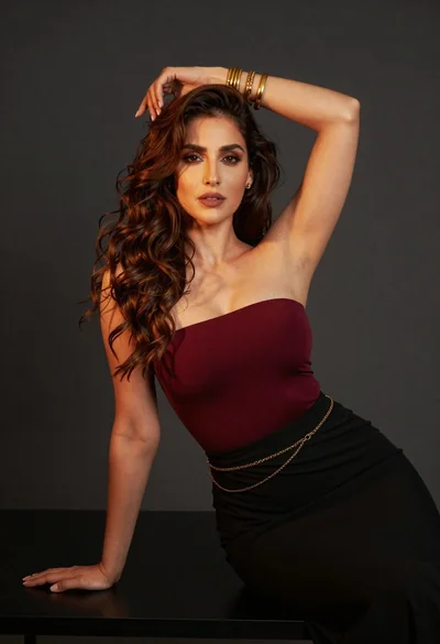 Confident woman with brown wavy hair in maroon top against dark background