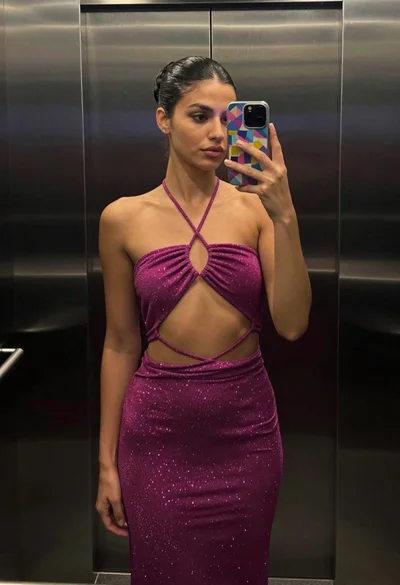 Woman taking mirror selfie in elevator wearing sparkly magenta cutout dress