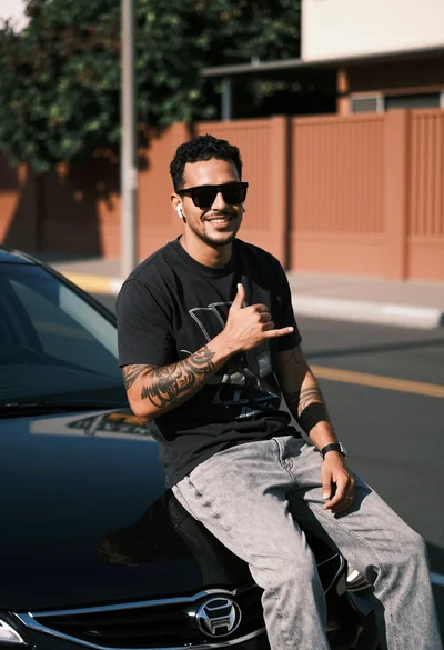 Smiling man with tattoos sitting on black car in urban street setting