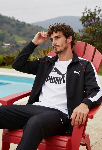Young man in black jacket sitting relaxed by swimming pool outdoors