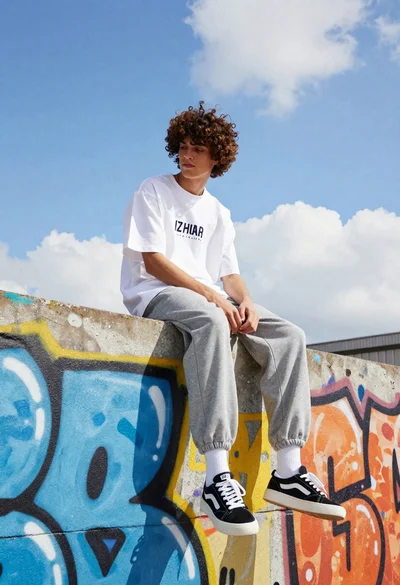 Young man with curly brown hair sitting on graffiti covered wall outdoors