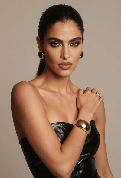 Dark skinned woman in black top posing with gold jewelry studio portrait