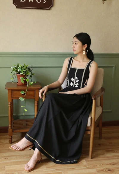 Woman sitting in wooden armchair with black embroidered top indoors