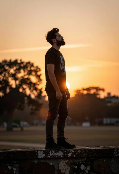 Man in black tshirt standing on wall against vibrant sunset sky