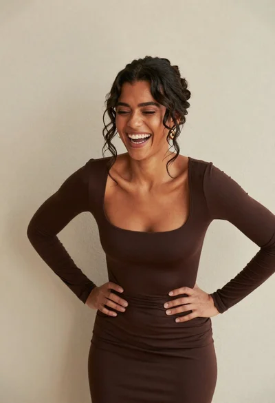 Laughing woman with dark wavy hair against a plain textured beige wall