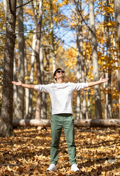 Man standing in sundrenched forest with arms outstretched showing joy