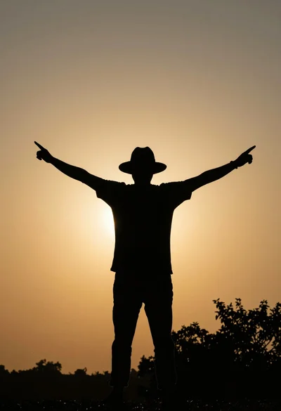Silhouetted figure with outstretched arms against vibrant golden sunset sky