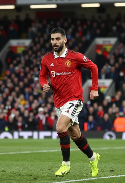 Football player running dynamically on green pitch under bright stadium lights
