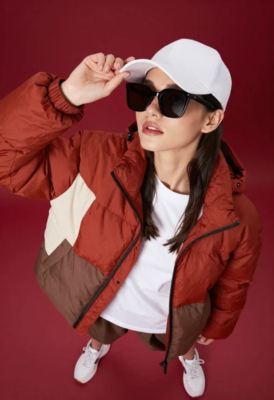 Stylish woman in colorblocked puffer jacket posing against deep red background