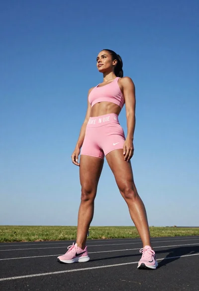 Fit woman in pink athletic wear standing on an asphalt track under