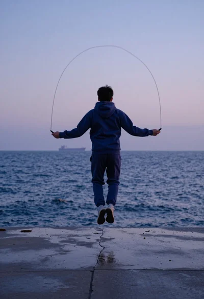 Person jumping rope on wet pier overlooking choppy blue ocean at dusk