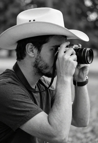 Man with cowboy hat holding vintage camera in profile portrait