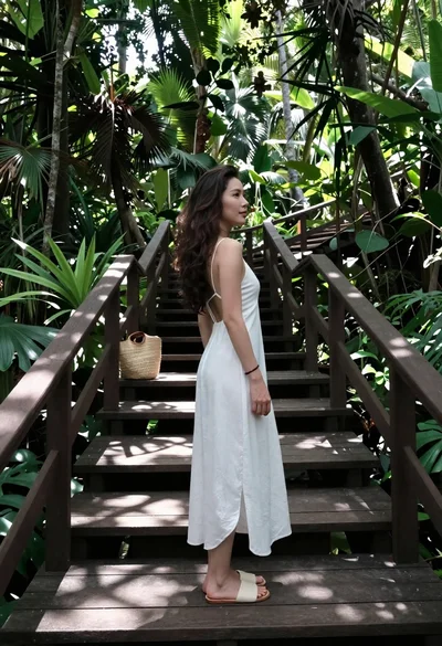Woman in white slip dress on wooden boardwalk through jungle foliage