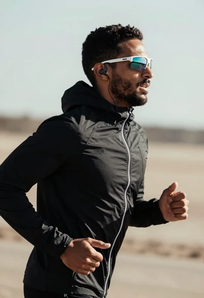 Fit man jogging outdoors in black jacket against blurred natural landscape