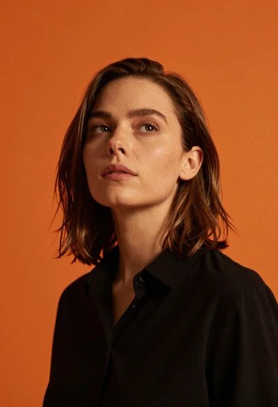 Woman with brown hair in black shirt looking up against orange background