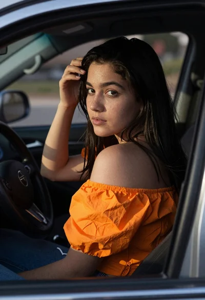 Young woman in orange top sitting inside car looking back over shoulder