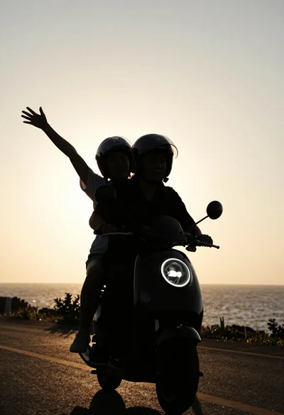 Two silhouetted figures riding scooter against golden sunset sky