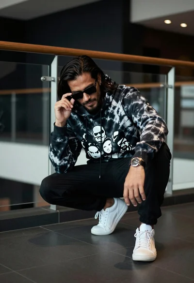 Man crouching in modern interior wearing tie dye hoodie by glass railing