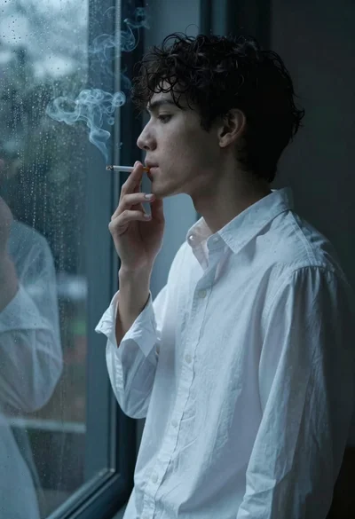 Medium close up profile of young man smoking by rainy window