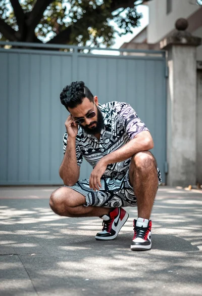 Man crouching on paved street near metal gate under dappled sunlight