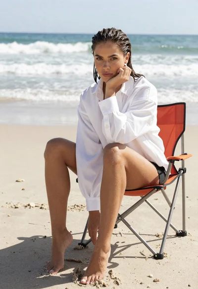 Woman sitting on beach chair with ocean background under bright sky