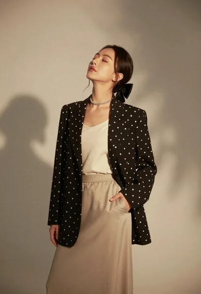 Woman in black blazer and beige skirt against textured studio backdrop
