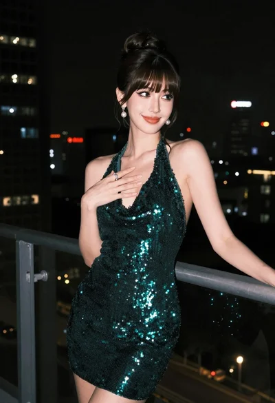 Glamorous woman in dark green sequined halter dress on balcony at night