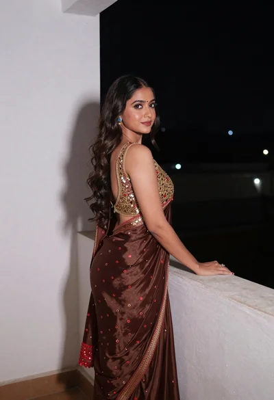 Young woman in brown saree posing elegantly on a night balcony