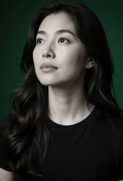 Portrait of woman with dark wavy hair looking left against deep green