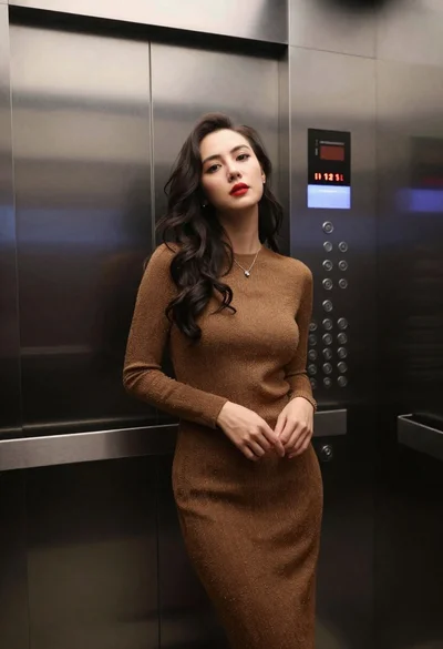 Woman in shimmering brown knit dress standing inside a modern elevator