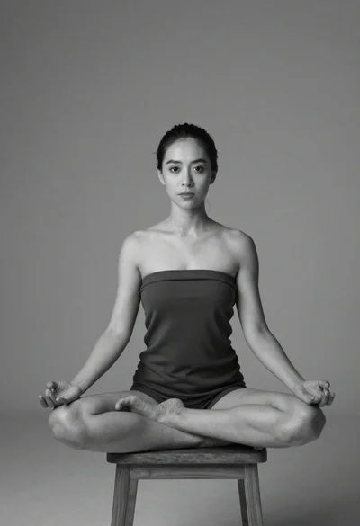 Woman in dark top meditating cross legged on wooden stool studio portrait