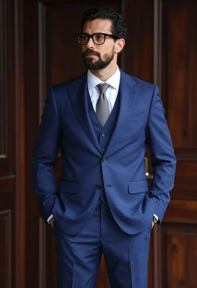 Handsome man in blue threepiece suit standing against dark wood paneling background