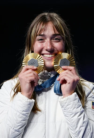 Joyful young woman holding gold medals against a solid black background