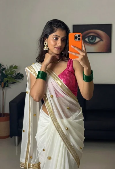 Young woman taking mirror selfie in white saree indoors