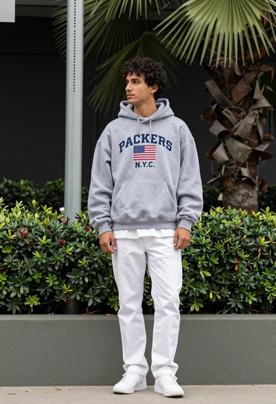 Man in grey hoodie leaning on low wall outdoors with green foliage
