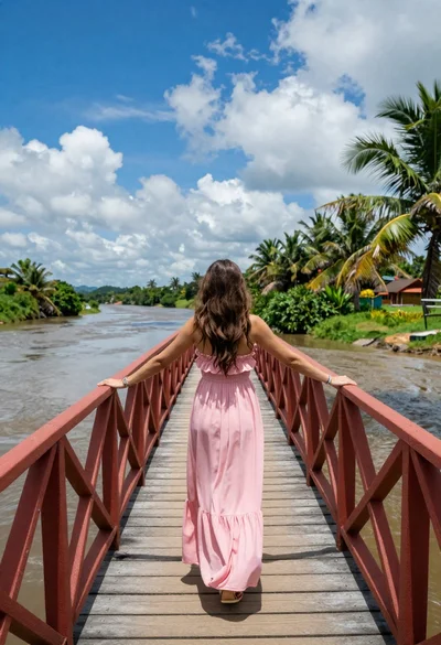 Woman in pink dress standing on wooden bridge overlooking river landscape