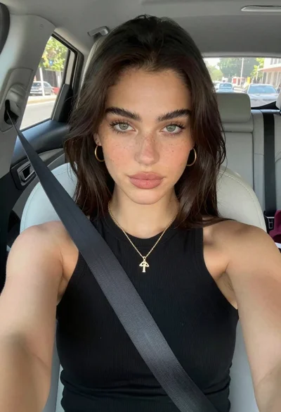 Young woman taking a selfie seated in a car interior during daylight