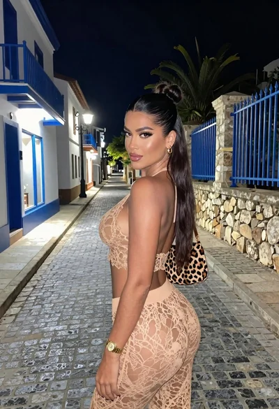Stylish woman looking back over shoulder on narrow cobblestone street at night