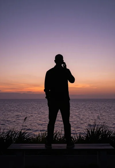 Silhouette of man on bench facing ocean during twilight hours